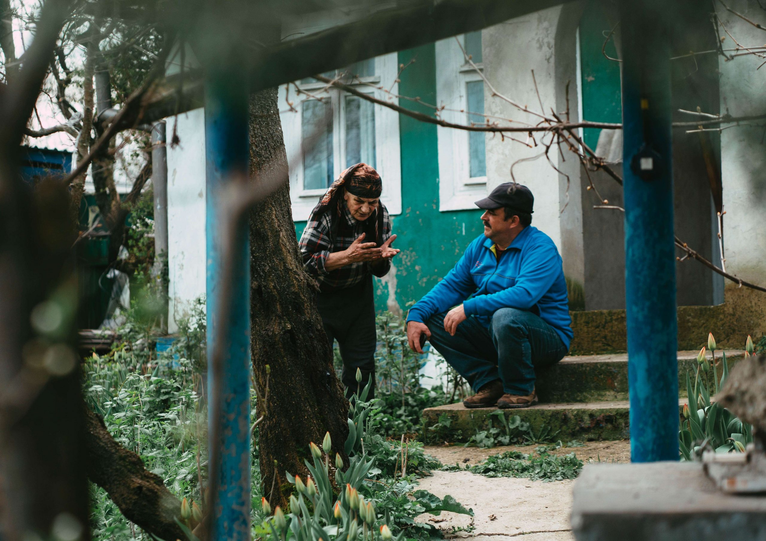 Ältere Frau spricht mit Mann, der auf einer Treppe sitzt.