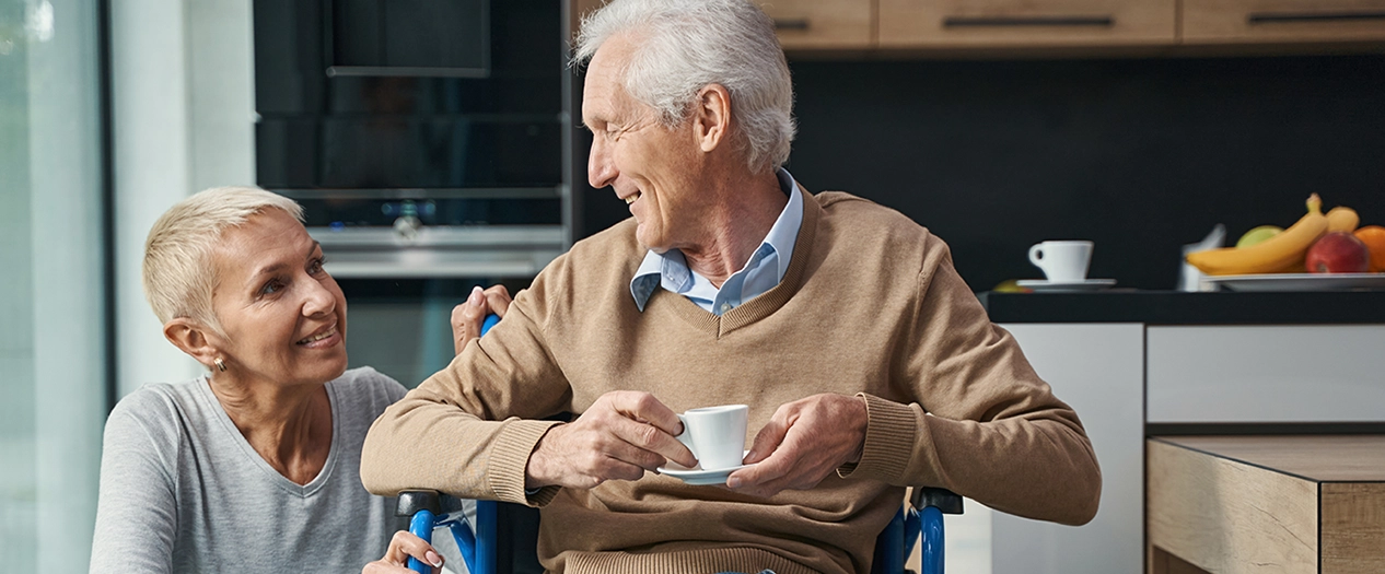 Mann sitzt Zuhause im Rollstuhl und hat eine Tasse Kaffee in der hand.