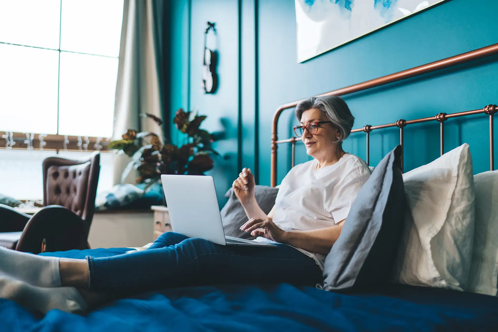 Seniorin liegt mit Laptop im Bett.