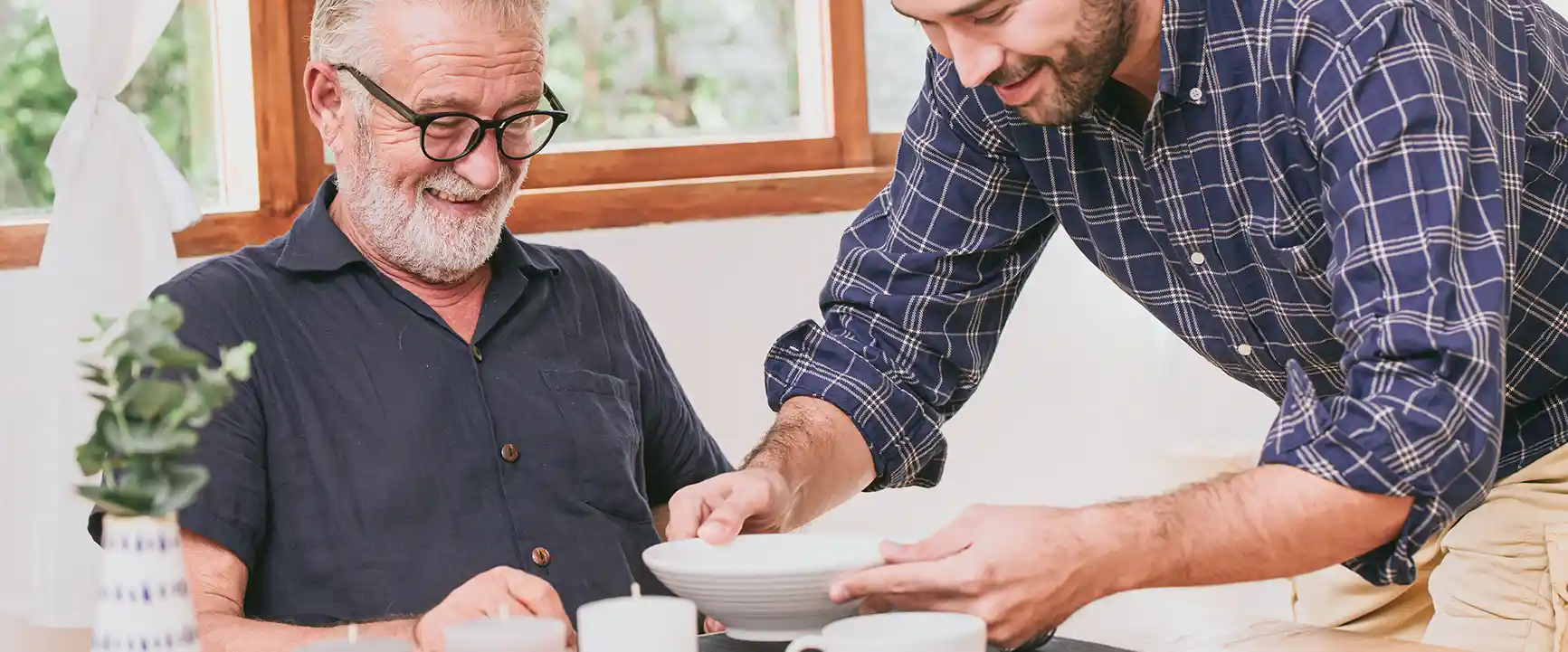 Ein junger Mann serviert einem Älteren Herrn das Essen.