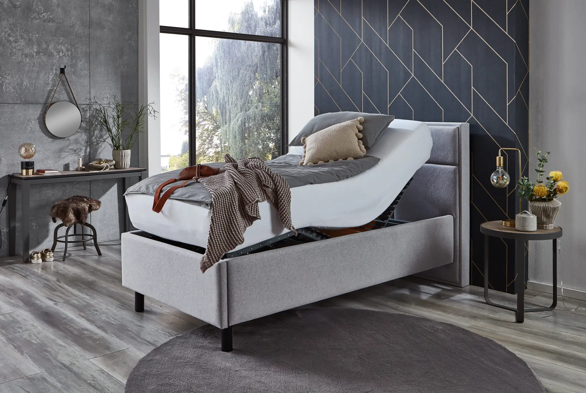 Elbacare Pflegebett mit beigen Stoffhussen und zweigeteiltem Aluminium-Seitengitter in einem modern eingerichteten Schlafzimmer – wohnliches, elektrisch verstellbares Pflegebett.